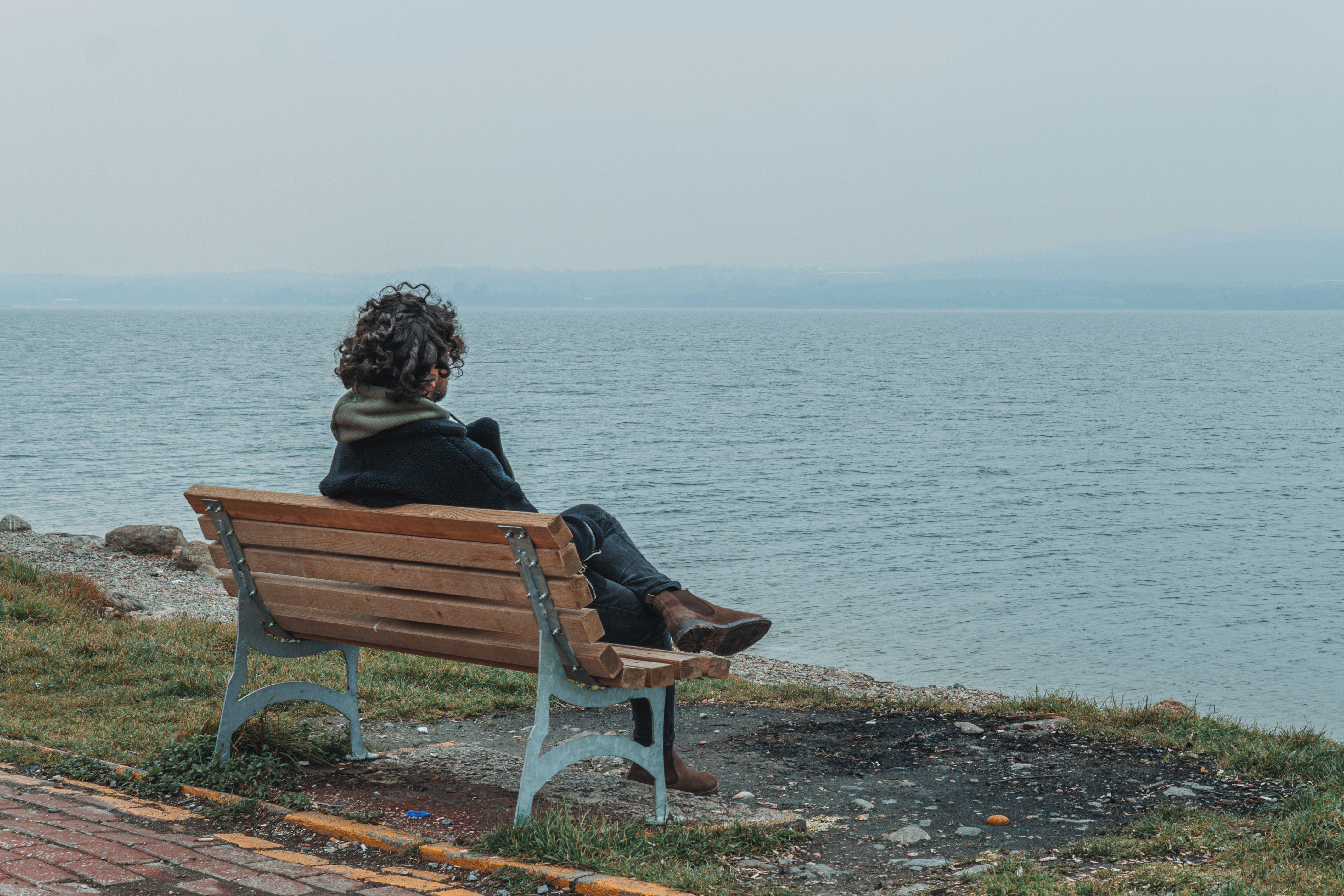 woman sitting on brown wooden bench near body of water during daytime